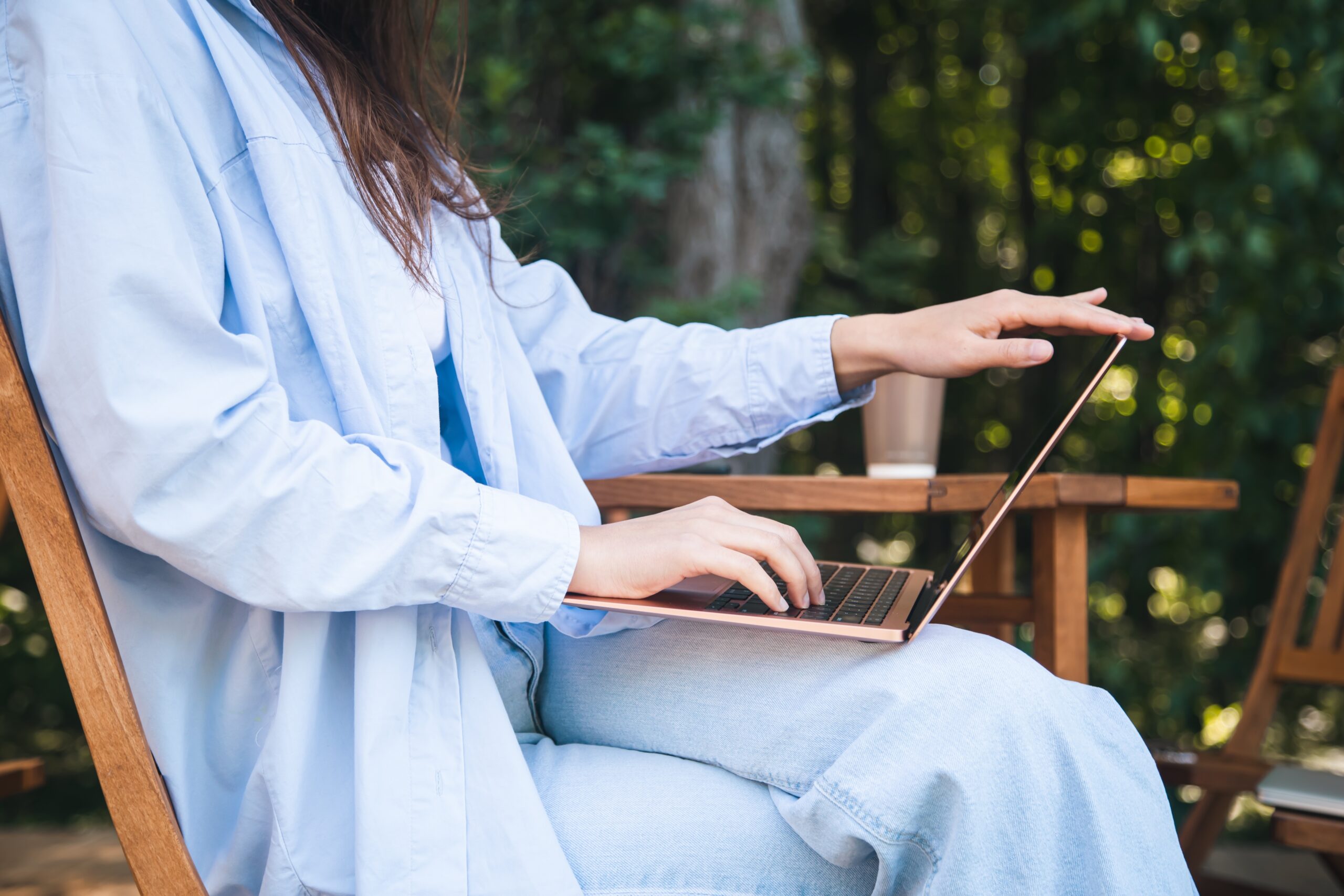 young woman in blue is working on her laptop while looking out at the forest